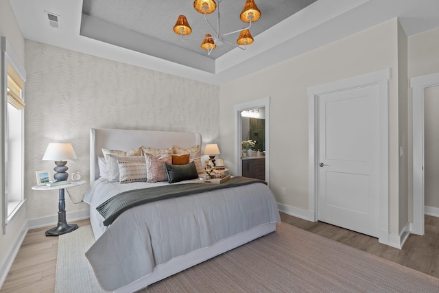 bedroom with baseboards, visible vents, a raised ceiling, and wood finished floors