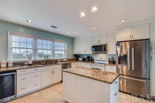 kitchen featuring beverage cooler, appliances with stainless steel finishes, a center island, stone counters, and white cabinetry