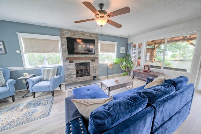 living room featuring light wood finished floors, baseboards, a textured ceiling, and a stone fireplace