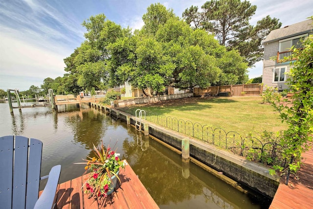 view of dock with a water view, boat lift, fence, and a lawn