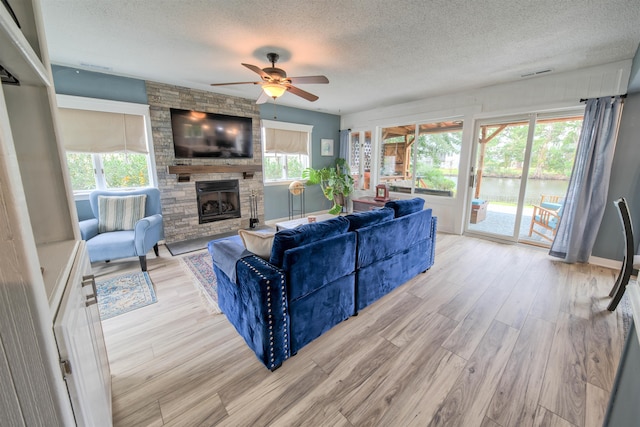 living area with a textured ceiling, ceiling fan, a fireplace, visible vents, and light wood-type flooring