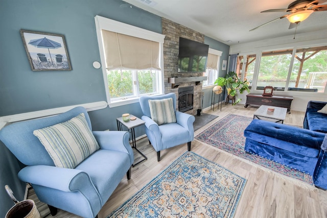 living room featuring ceiling fan, a stone fireplace, and light wood-type flooring