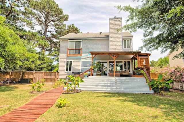 rear view of house with a yard, a chimney, ceiling fan, a fenced backyard, and a wooden deck