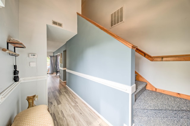 hallway featuring wood finished floors, visible vents, a towering ceiling, and stairs