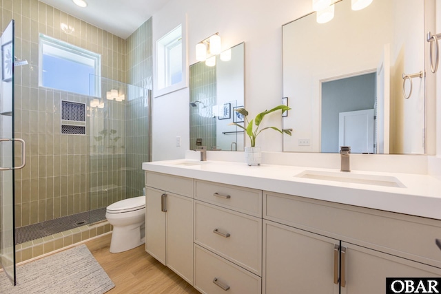 bathroom with double vanity, toilet, a sink, a shower stall, and wood finished floors