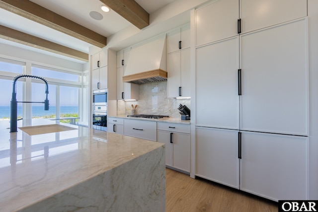 kitchen featuring premium range hood, a sink, appliances with stainless steel finishes, beam ceiling, and decorative backsplash