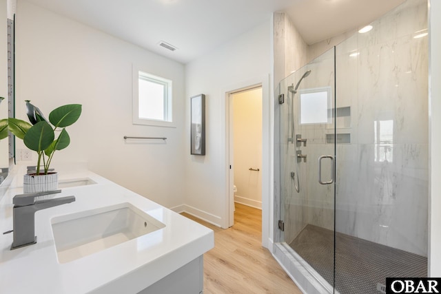 full bath with a marble finish shower, visible vents, toilet, wood finished floors, and a sink