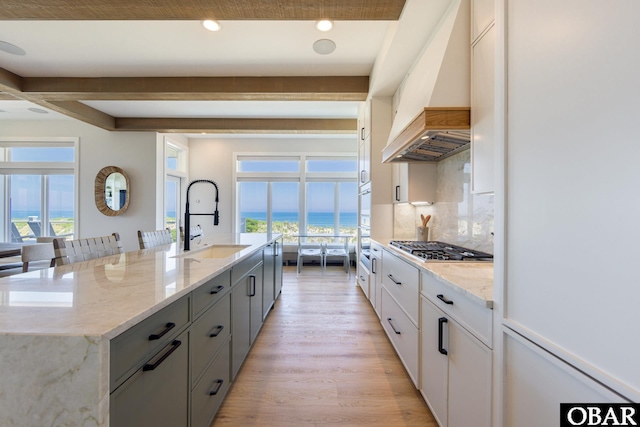 kitchen featuring a sink, light wood-style floors, custom exhaust hood, beam ceiling, and decorative backsplash