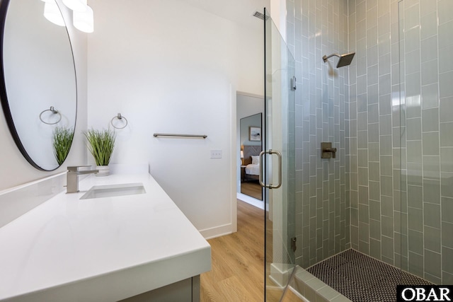 ensuite bathroom featuring connected bathroom, vanity, wood finished floors, baseboards, and a walk in shower