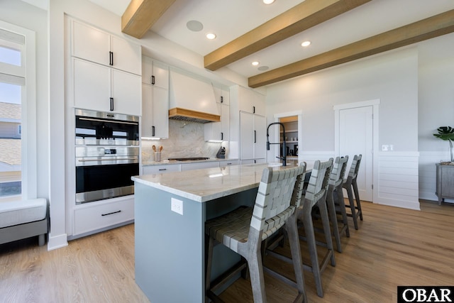 kitchen featuring a kitchen breakfast bar, custom exhaust hood, stainless steel double oven, gas stovetop, and beam ceiling