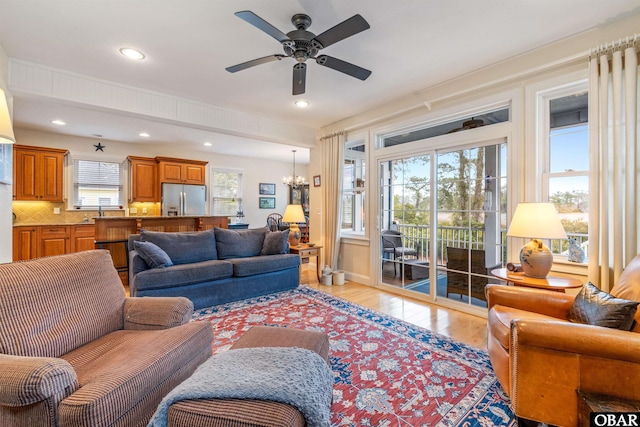 living area with light wood-style floors, recessed lighting, and ceiling fan with notable chandelier