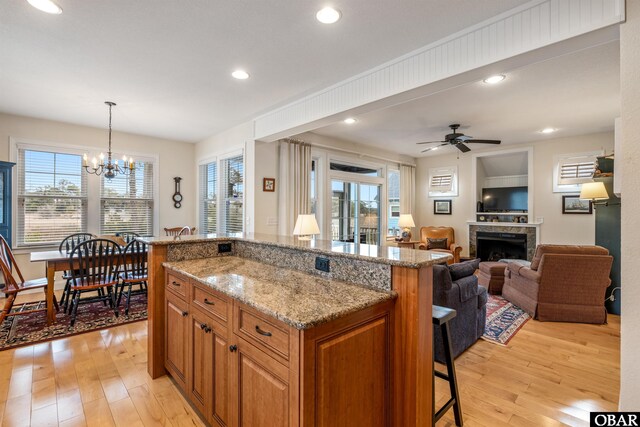 kitchen with brown cabinetry, light stone counters, a breakfast bar, open floor plan, and decorative light fixtures