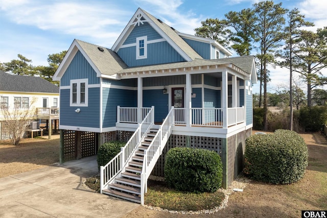 raised beach house featuring roof with shingles, covered porch, stairway, a carport, and driveway