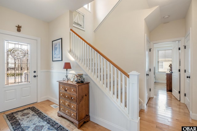 foyer with light wood-type flooring, wainscoting, visible vents, and stairs