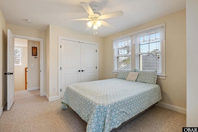 bedroom with light carpet, a ceiling fan, baseboards, and a closet