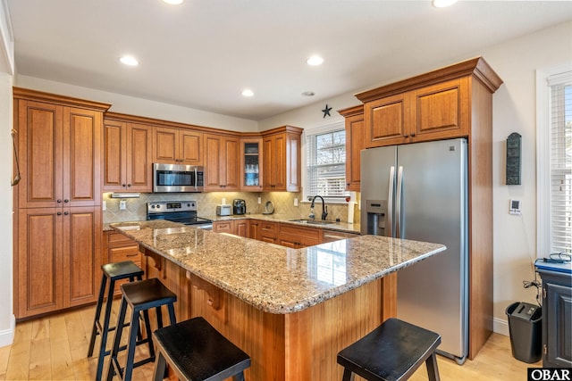 kitchen featuring stainless steel appliances, a breakfast bar area, light stone countertops, and brown cabinets