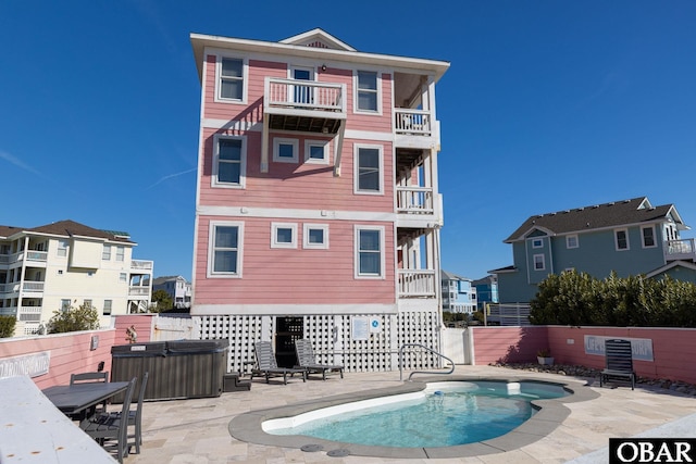 back of house with a fenced in pool, a fenced backyard, a hot tub, and a balcony