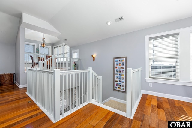 hallway with dark wood-style floors, lofted ceiling, visible vents, an upstairs landing, and baseboards