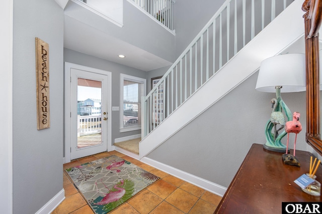 foyer entrance with stairs, light tile patterned flooring, and baseboards