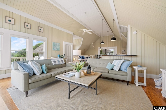 living area featuring ceiling fan, wooden walls, light wood-type flooring, and vaulted ceiling with beams