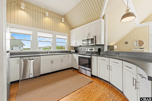 kitchen featuring light wood finished floors, a sink, dark countertops, appliances with stainless steel finishes, and vaulted ceiling