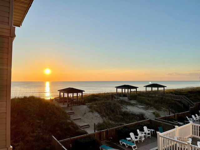 dock area with a gazebo, a water view, and a view of the beach