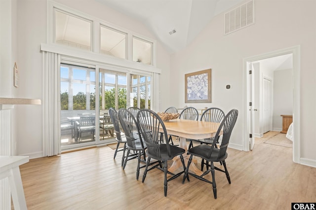 dining space featuring light wood-style floors, baseboards, and high vaulted ceiling