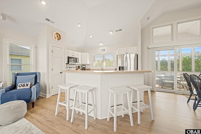 kitchen featuring appliances with stainless steel finishes, open floor plan, a kitchen breakfast bar, white cabinetry, and high vaulted ceiling