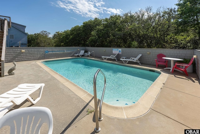 view of pool with a patio, fence, and view of wooded area