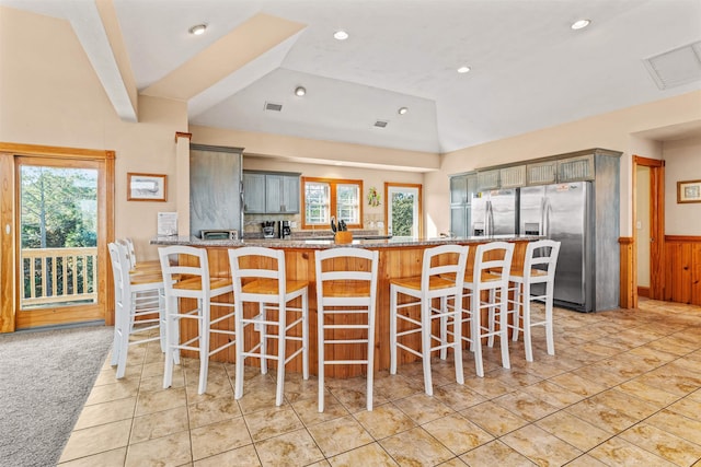 kitchen with visible vents, stainless steel fridge with ice dispenser, a peninsula, light stone countertops, and vaulted ceiling