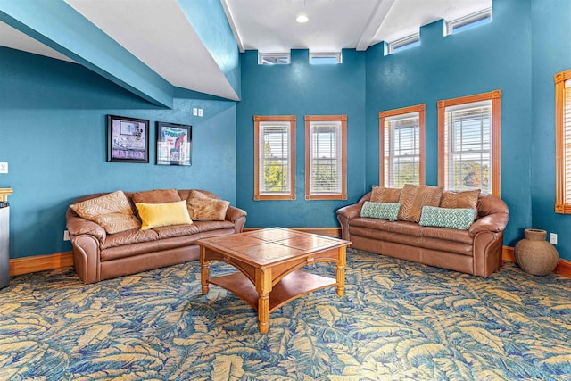 living area with a healthy amount of sunlight, carpet flooring, beamed ceiling, and baseboards