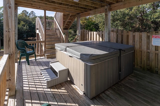 wooden terrace with a hot tub, stairs, and fence