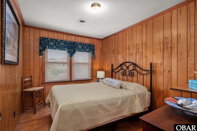 bedroom with wooden walls, a textured ceiling, visible vents, and wood finished floors