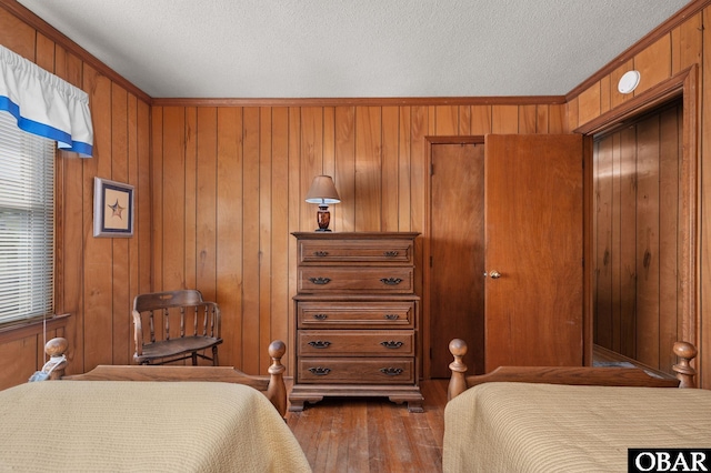 bedroom featuring wooden walls, crown molding, a textured ceiling, and wood finished floors