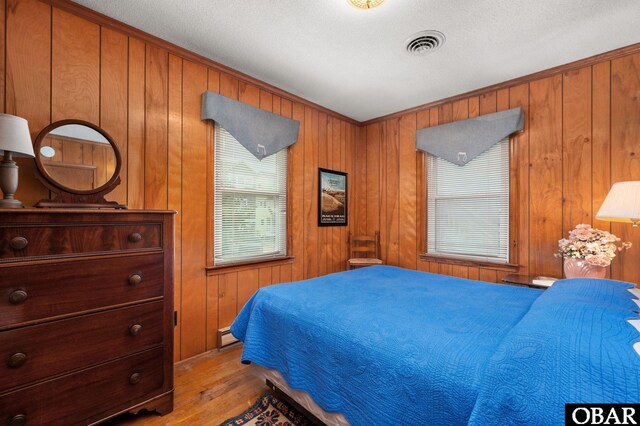 bedroom with light wood finished floors, multiple windows, a baseboard radiator, and visible vents