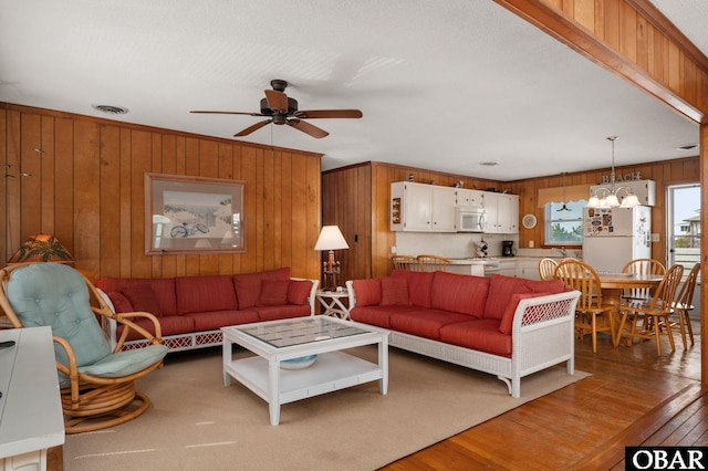 living area featuring ceiling fan with notable chandelier, wood walls, wood finished floors, and visible vents