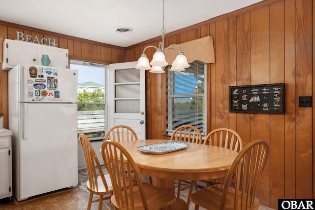 dining room with an inviting chandelier, wooden walls, and visible vents