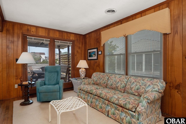 living room with crown molding, visible vents, wood walls, and wood finished floors