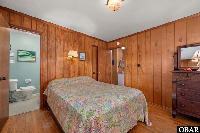 bedroom featuring connected bathroom, wood walls, ornamental molding, and wood finished floors