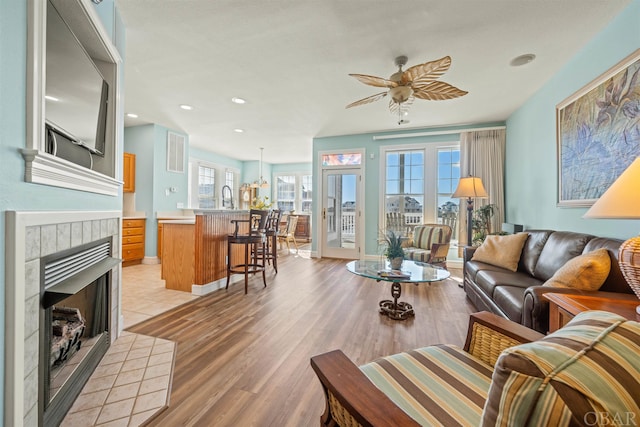 living area with light wood-style flooring, ceiling fan, a tiled fireplace, and recessed lighting