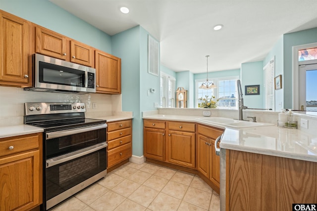 kitchen with brown cabinets, decorative light fixtures, a peninsula, stainless steel appliances, and backsplash