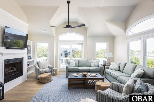 living area featuring light wood-type flooring, a large fireplace, visible vents, and a healthy amount of sunlight