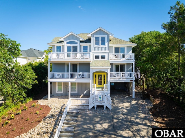 coastal home with board and batten siding, concrete driveway, roof with shingles, and a balcony