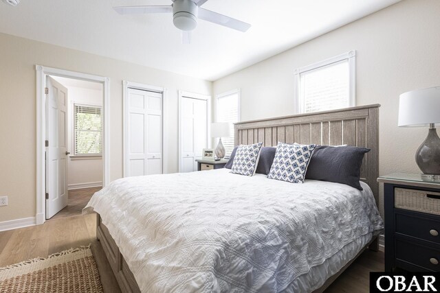 bedroom with multiple closets, ceiling fan, baseboards, and dark wood-style floors