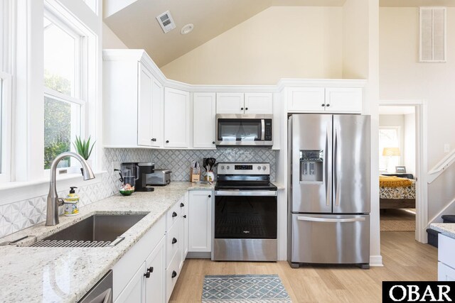 kitchen with light stone counters, stainless steel appliances, a sink, visible vents, and white cabinets