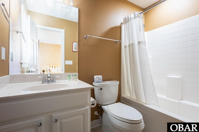 bathroom with toilet, a textured wall, shower / bathtub combination with curtain, and vanity