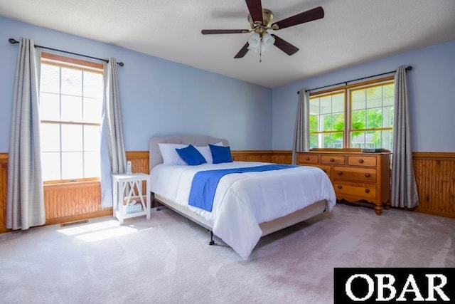128 Daphne Ln Lot 17, Manteo, NC 27954 - carpeted bedroom featuring wainscoting, multiple windows, wooden walls, a ceiling fan, and a textured ceiling