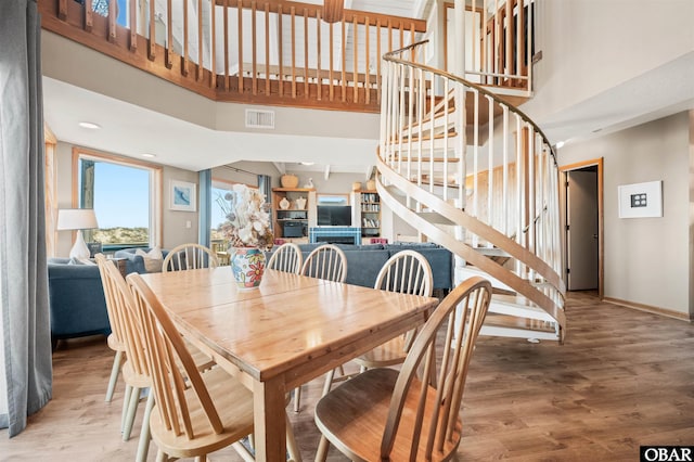 dining area featuring visible vents, a towering ceiling, wood finished floors, baseboards, and stairs