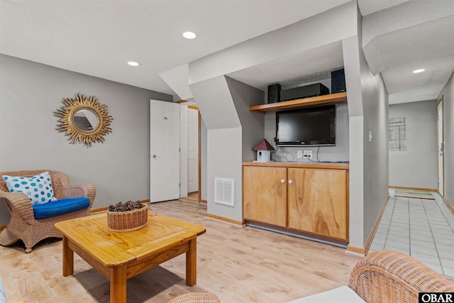 living area with light wood-style floors, recessed lighting, visible vents, and baseboards