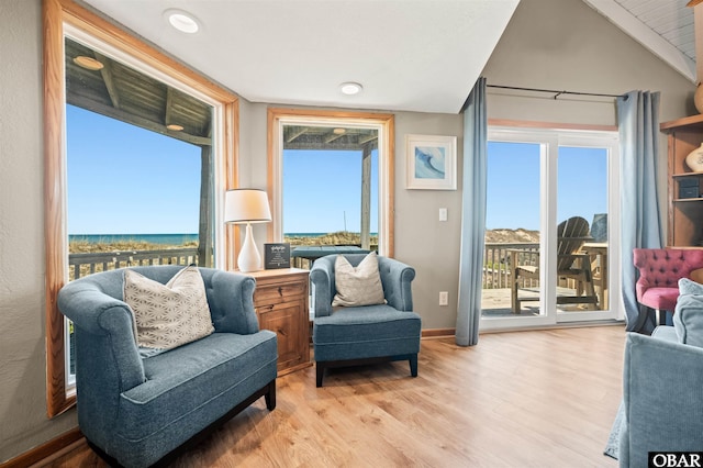 sitting room with a water view, plenty of natural light, vaulted ceiling, and light wood-style flooring